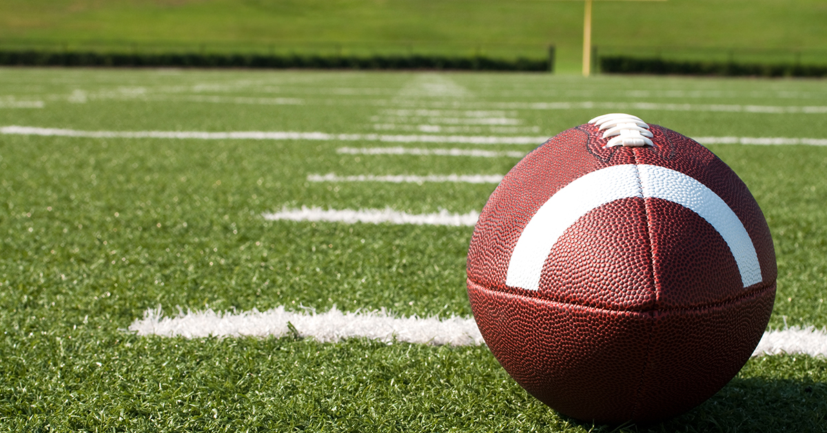 Closeup of American football on field with yard lines.