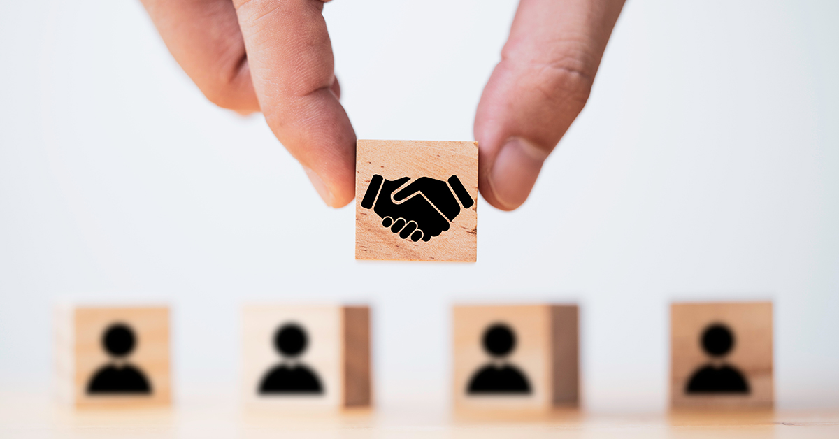 Hand holding wooden cube which drawing of hand shaking print screen on wooden cube block  in front of human icon for business deal and agreement concept.