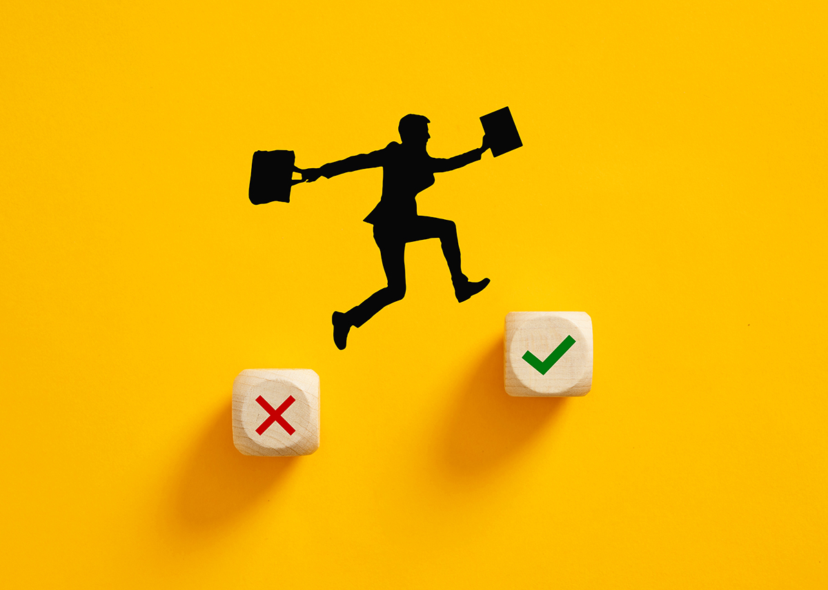 Choosing the right way, making the right decision in business. Making up for a mistake. Silhouette of a businessman jumping from wrong cross symbol to right check mark symbol on wooden cubes.
