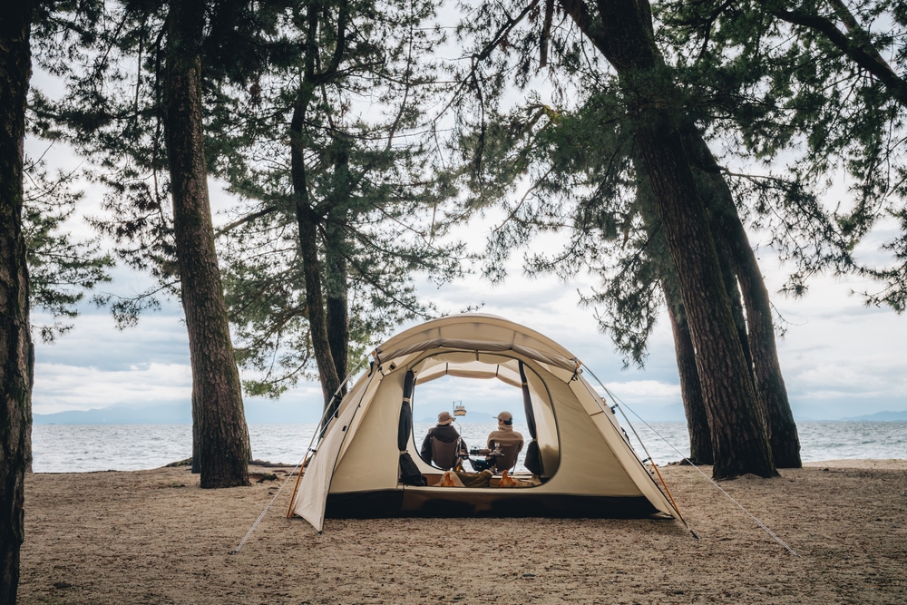 Man and woman sit outside of a tent in the woods